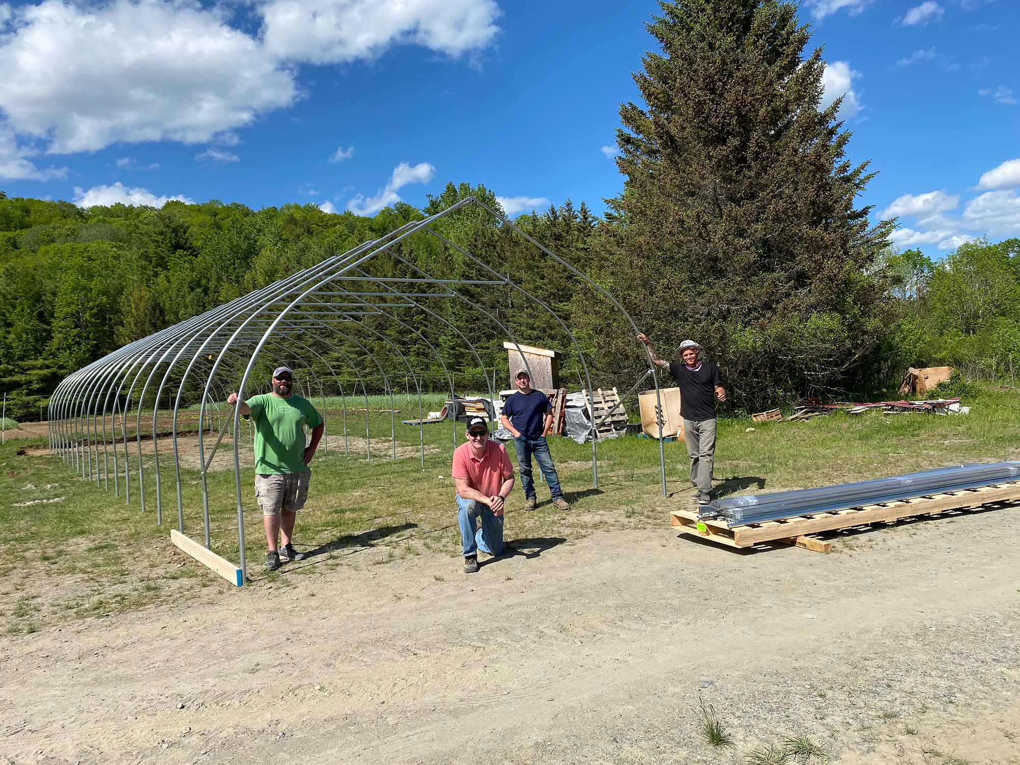 A group of volunteers are outside with greenhouse framing behind them.