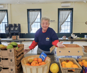 A smiling woman gestures to a display of citrus fruit on a table