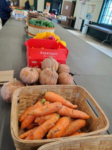 Baskets and boxes of carrots, squash, peppers, and broccoli displayed on folding tables.