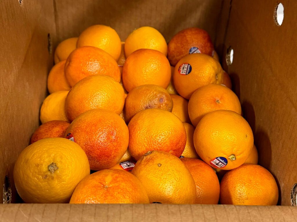 A close-up photo oranges in a cardboard box.
