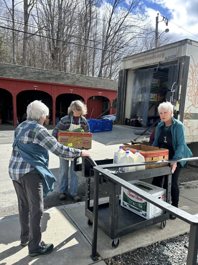 Three women unload food from a Willing Hands box truck using a hand cart