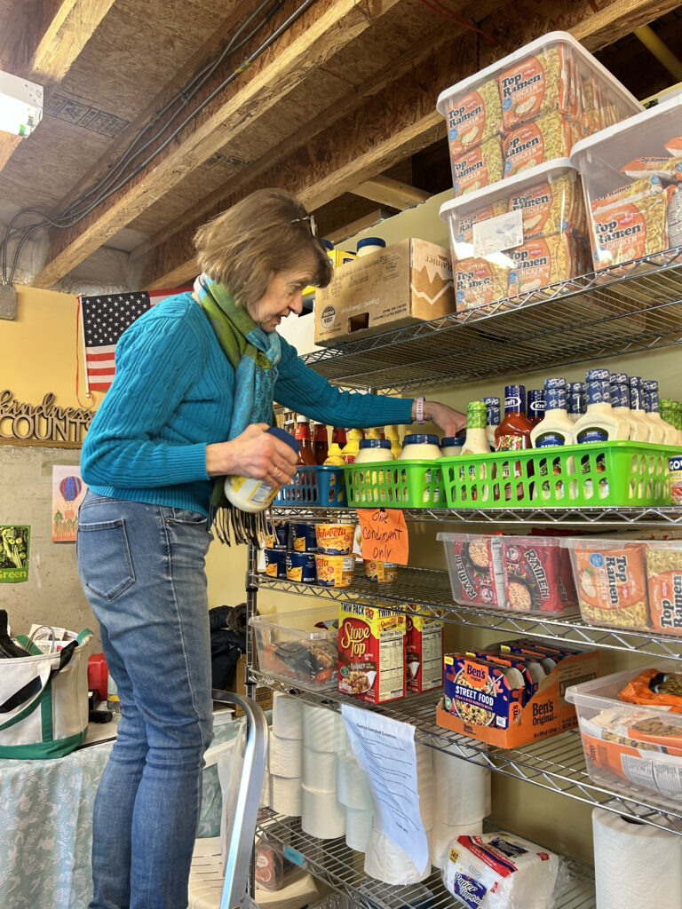  woman stands on a step ladder to stock shelves of food