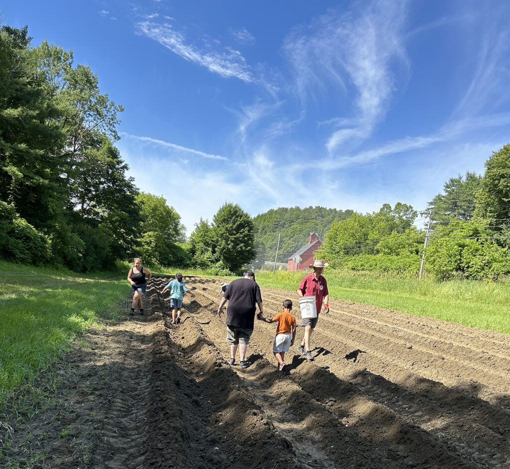 A group of adults and children walk through recently tilled farm fields.